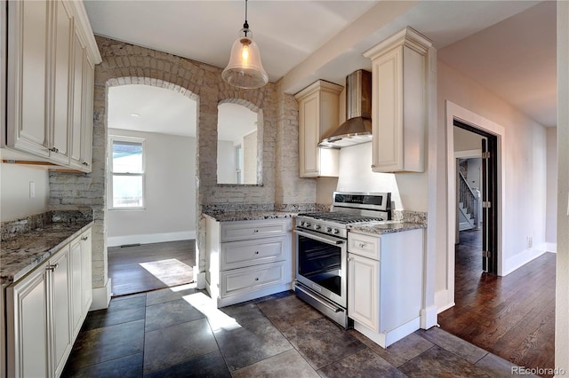 kitchen with stone counters, cream cabinets, wall chimney exhaust hood, decorative light fixtures, and stainless steel range with gas stovetop