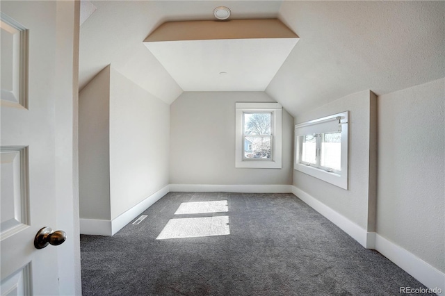 additional living space featuring dark carpet and vaulted ceiling