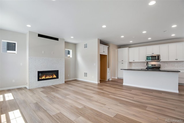 kitchen featuring white cabinets, a tiled fireplace, stainless steel appliances, light hardwood / wood-style floors, and decorative backsplash