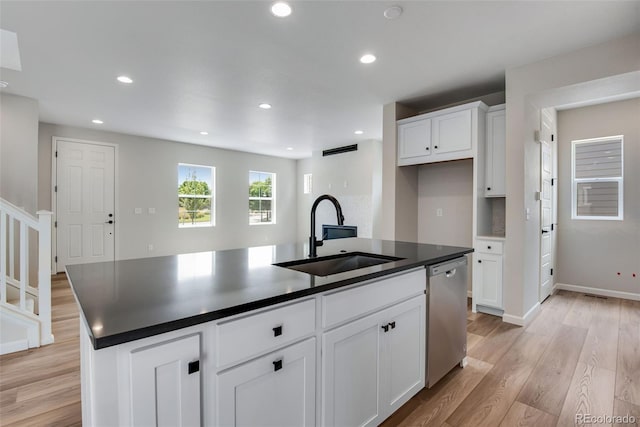 kitchen with dishwasher, a kitchen island with sink, sink, white cabinetry, and light wood-type flooring