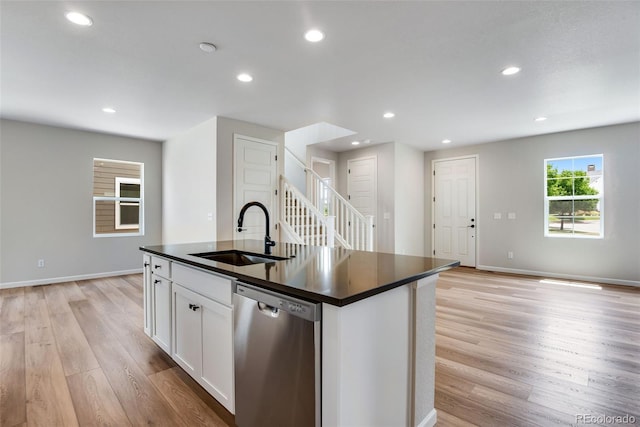 kitchen featuring light wood-type flooring, an island with sink, sink, stainless steel dishwasher, and white cabinets