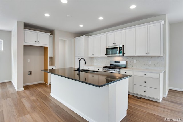 kitchen featuring light hardwood / wood-style flooring, appliances with stainless steel finishes, white cabinetry, sink, and a center island with sink