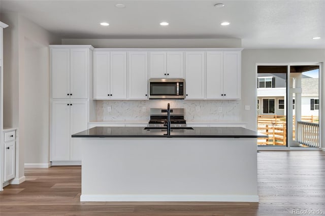 kitchen with light hardwood / wood-style flooring, a kitchen island with sink, stainless steel appliances, sink, and white cabinets