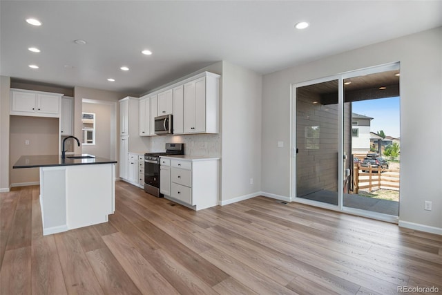 kitchen featuring appliances with stainless steel finishes, light hardwood / wood-style floors, white cabinetry, sink, and a center island with sink