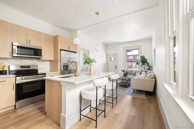 kitchen with stainless steel appliances, light countertops, an island with sink, a kitchen bar, and decorative light fixtures