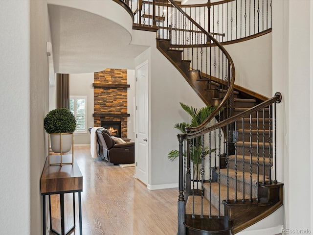 stairs with a fireplace, wood finished floors, a towering ceiling, and baseboards