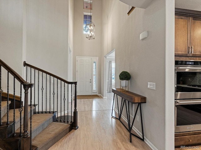 entryway featuring light wood finished floors, baseboards, a towering ceiling, an inviting chandelier, and stairs