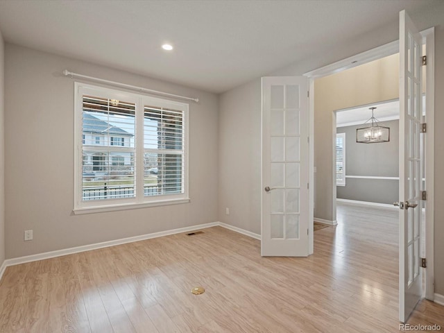 empty room with french doors, a notable chandelier, visible vents, light wood-style floors, and baseboards