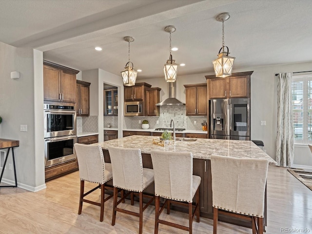 kitchen with decorative light fixtures, a large island, stainless steel appliances, tasteful backsplash, and wall chimney range hood