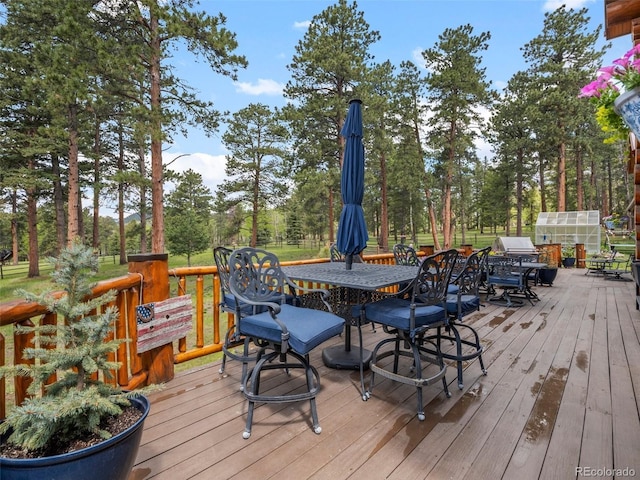 23076 Oehlmann Park Rd, Conifer, CO 80433 - wooden terrace featuring outdoor dining space, view of wooded area, and an exterior structure