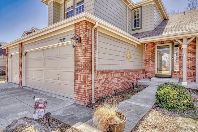 doorway to property with a garage, driveway, roof with shingles, and brick siding