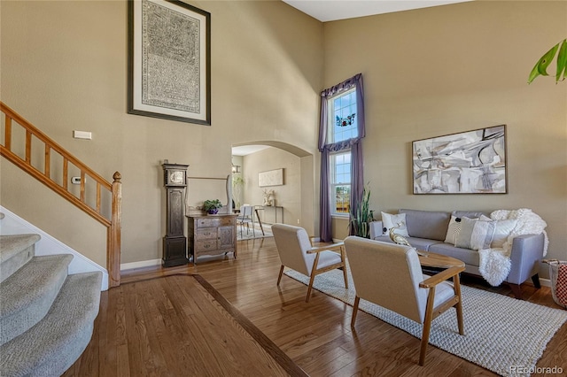 living room with arched walkways, wood-type flooring, a high ceiling, baseboards, and stairs