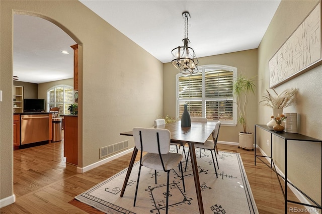 dining room with arched walkways, baseboards, visible vents, and light wood-style floors