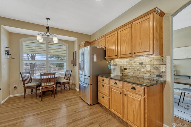 kitchen featuring tasteful backsplash, dark stone countertops, stainless steel fridge, and light wood-style flooring