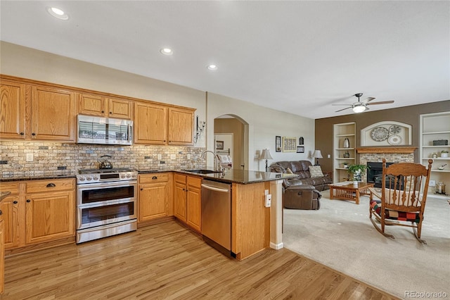 kitchen with arched walkways, open floor plan, stainless steel appliances, a fireplace, and a sink