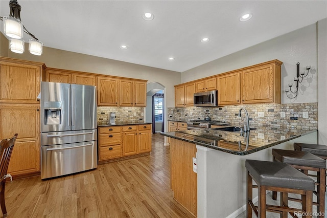 kitchen with arched walkways, appliances with stainless steel finishes, dark stone countertops, light wood-style floors, and a sink