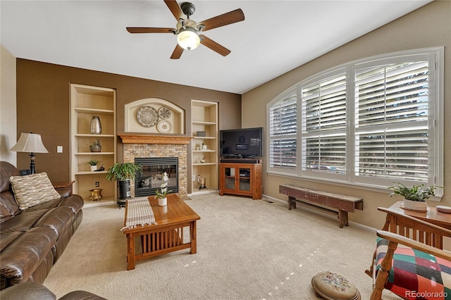 carpeted living area with built in shelves, a glass covered fireplace, a ceiling fan, and baseboards