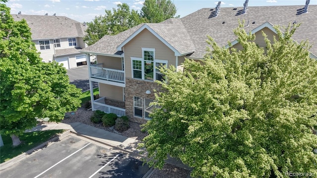 rear view of house featuring stone siding, a balcony, uncovered parking, and roof with shingles
