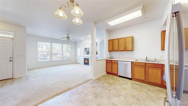 kitchen with stainless steel dishwasher, light carpet, a sink, a warm lit fireplace, and light countertops