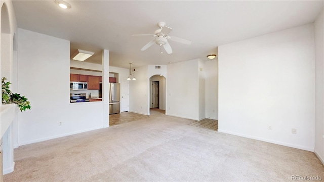 unfurnished living room featuring arched walkways, a ceiling fan, light carpet, and baseboards