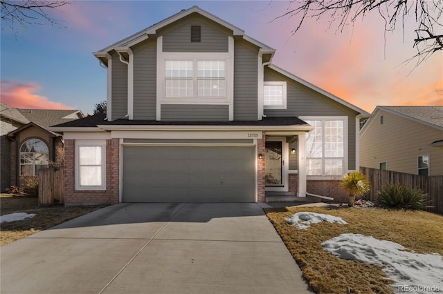 traditional-style home featuring driveway, brick siding, an attached garage, and fence