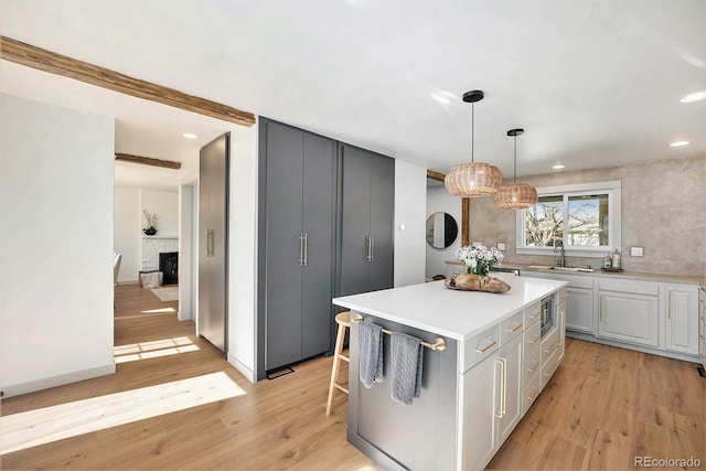 kitchen with a sink, stainless steel microwave, light countertops, and light wood-style floors