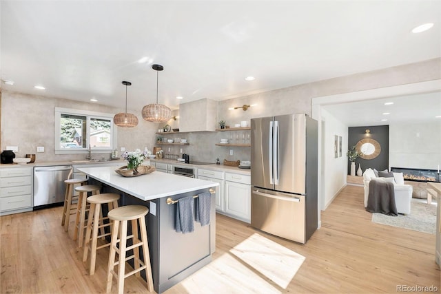 kitchen with light wood finished floors, stainless steel appliances, open shelves, and light countertops