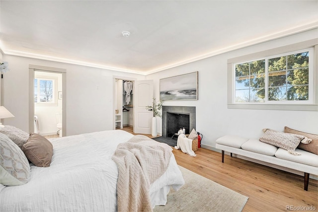 bedroom featuring baseboards, a tiled fireplace, connected bathroom, and wood finished floors