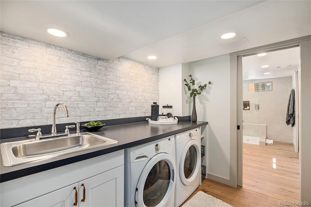 clothes washing area featuring a sink, independent washer and dryer, recessed lighting, light wood finished floors, and brick wall