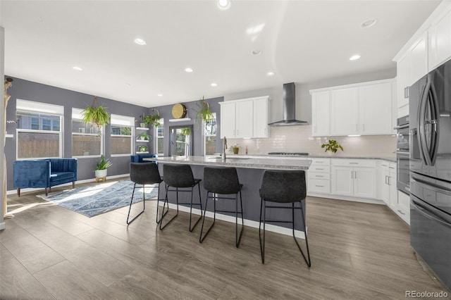 118 N Newcastle Way, Aurora, CO 80018 - kitchen with wall chimney exhaust hood, freestanding refrigerator, gas stovetop, a breakfast bar, and backsplash