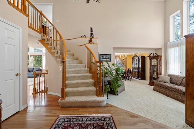 staircase with a towering ceiling, an inviting chandelier, hardwood / wood-style flooring, and a wealth of natural light