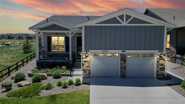 view of front facade featuring concrete driveway, stone siding, roof with shingles, covered porch, and board and batten siding