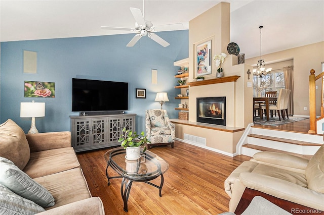 living room featuring vaulted ceiling, ceiling fan with notable chandelier, and hardwood / wood-style floors