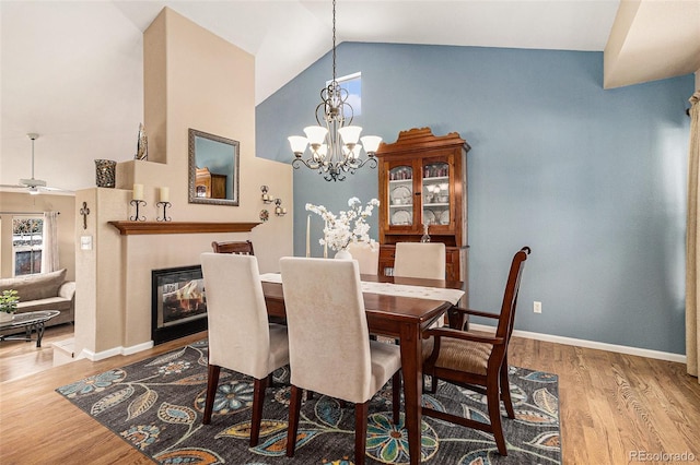 dining room with ceiling fan with notable chandelier, high vaulted ceiling, and light hardwood / wood-style floors