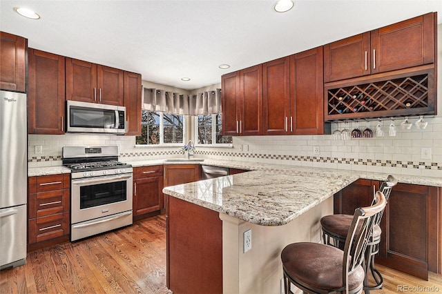 kitchen featuring sink, a breakfast bar area, light stone counters, appliances with stainless steel finishes, and hardwood / wood-style flooring