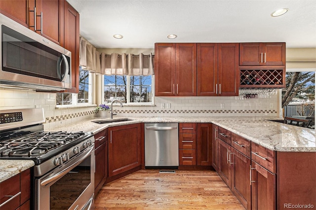 kitchen featuring tasteful backsplash, sink, stainless steel appliances, light stone countertops, and light wood-type flooring