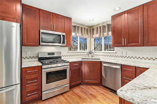 kitchen featuring sink, stainless steel appliances, light stone counters, light hardwood / wood-style floors, and decorative backsplash