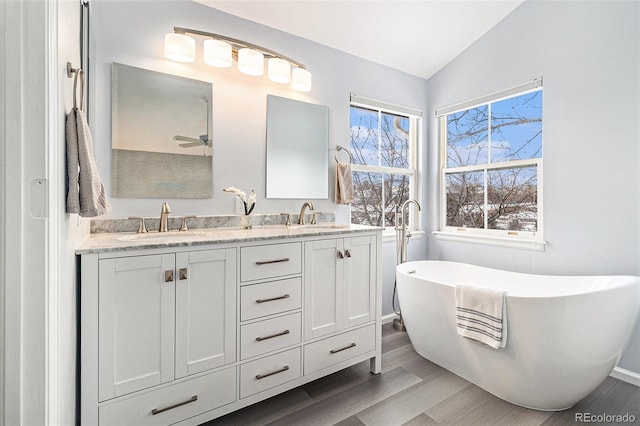 bathroom featuring lofted ceiling, ceiling fan, vanity, wood-type flooring, and a tub to relax in