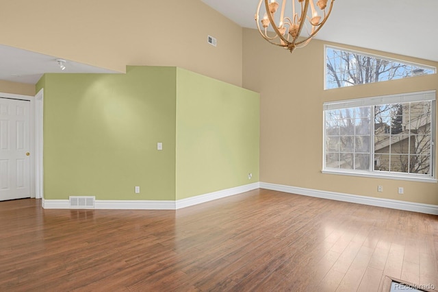 unfurnished room featuring baseboards, wood finished floors, visible vents, and an inviting chandelier