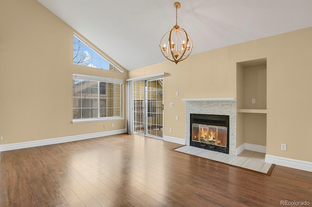 unfurnished living room featuring an inviting chandelier, a fireplace with flush hearth, wood finished floors, high vaulted ceiling, and baseboards