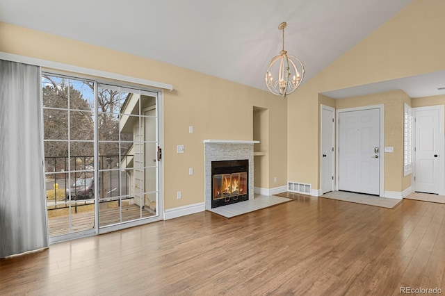 unfurnished living room with visible vents, a glass covered fireplace, wood finished floors, vaulted ceiling, and a notable chandelier