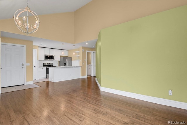 unfurnished living room with baseboards, high vaulted ceiling, wood finished floors, and a notable chandelier