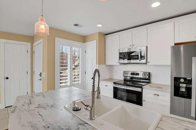 kitchen featuring a sink, visible vents, white cabinetry, hanging light fixtures, and appliances with stainless steel finishes