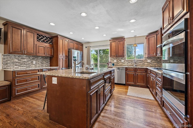 10714 Birch Ct, Thornton, CO 80233 - kitchen with stainless steel appliances, wood finished floors, a center island with sink, recessed lighting, and tasteful backsplash