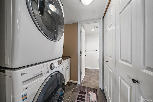 10714 Birch Ct, Thornton, CO 80233 - washroom with stacked washer and clothes dryer, cabinet space, a textured ceiling, and dark stone finish floors