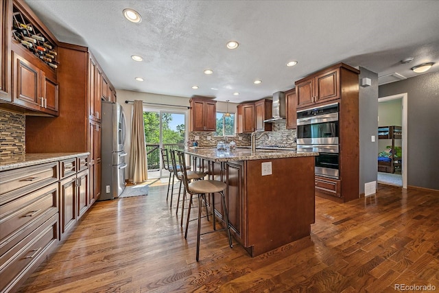 10714 Birch Ct, Thornton, CO 80233 - kitchen with stainless steel appliances, wall chimney range hood, a kitchen island with sink, recessed lighting, and tasteful backsplash