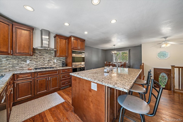 10714 Birch Ct, Thornton, CO 80233 - kitchen with wall chimney exhaust hood, appliances with stainless steel finishes, dark wood-style floors, a center island with sink, and tasteful backsplash
