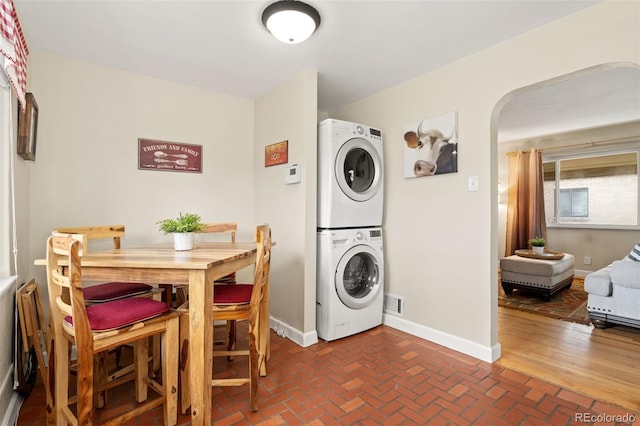 1432 Xanthia St, Denver, CO 80220 - laundry area featuring stacked washer and clothes dryer, arched walkways, baseboards, and brick flooring