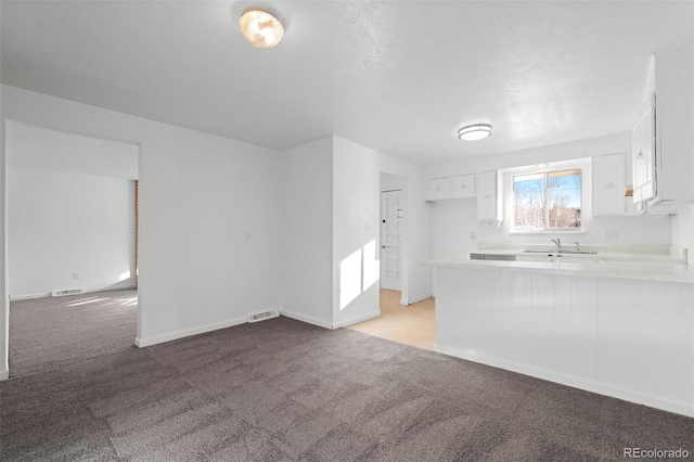 kitchen with sink, light carpet, white cabinets, and kitchen peninsula