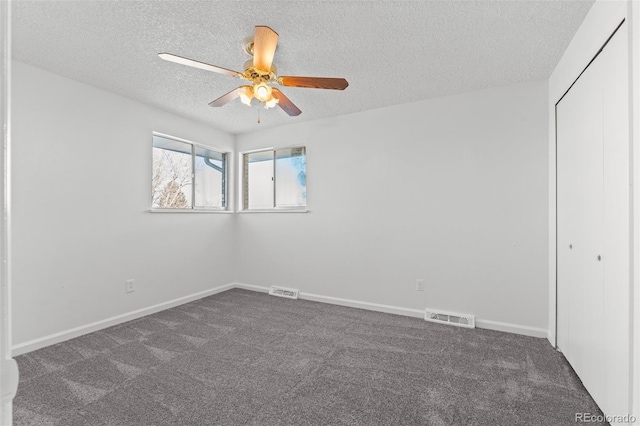 unfurnished bedroom with ceiling fan, a closet, a textured ceiling, and dark colored carpet